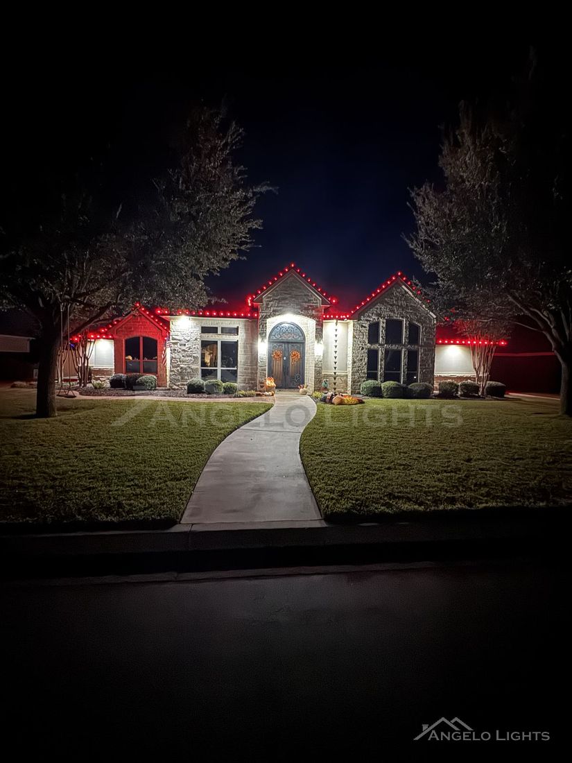 Stone home lit in red permanent lighting with a front walkway