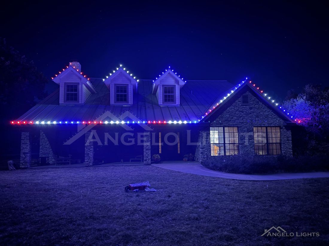 Red, white and blue permanent lights on a stone home with dormers