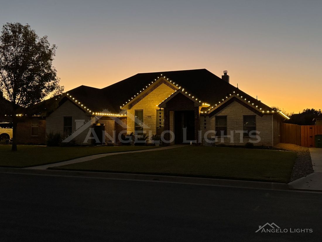 Warm white roofline lights on a stone home at sunset