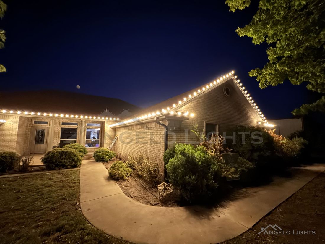 Warm white lights along the roofline and front walk of a San Angelo home